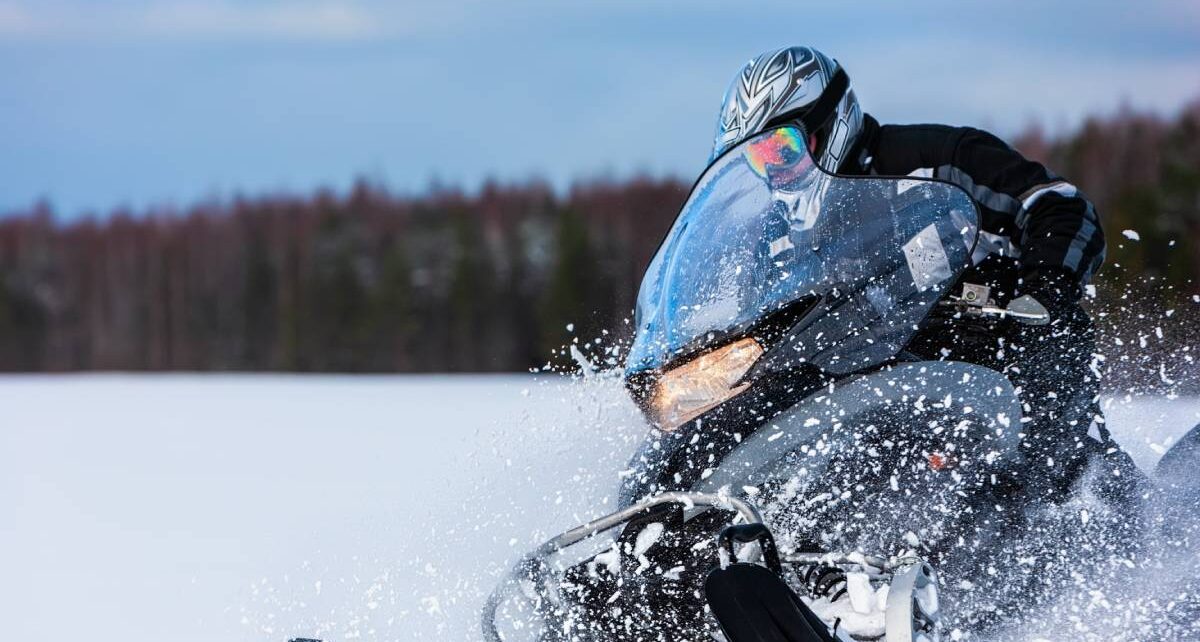 How To Enjoy the Snow Even if You Hate It 1 A snowmobile rider out in the backcountry in full cold-weather gear. They're turning the machine to splash snow.