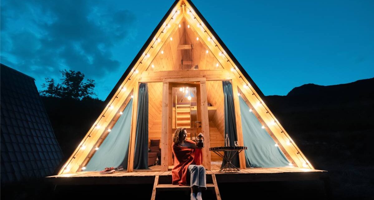 How To Connect With Nature Without Compromising Comfort 1 A woman sitting on the porch of an outdoor glamping tent. The tent is lit up and the night sky is slightly cloudy.