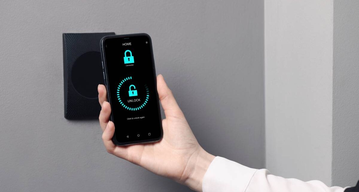 What To Know About the Future of Keyless Access Solutions 3 A woman holds a smartphone up to an access point. The phone says "Home" at the top of the screen and "Unlock" in the middle.