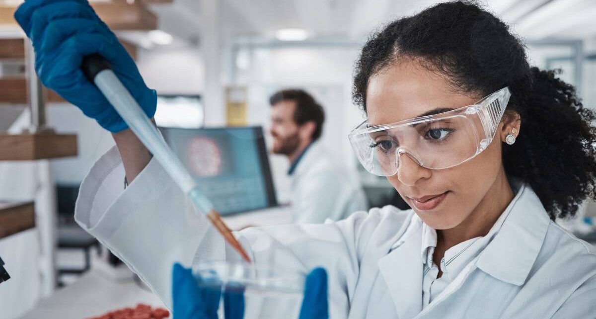 Tips To Ensure a Safe and Efficient Lab Environment 1 Female scientist wearing white robe, safety goggles, and blue latex gloves, holding a pipette over a petri dish.