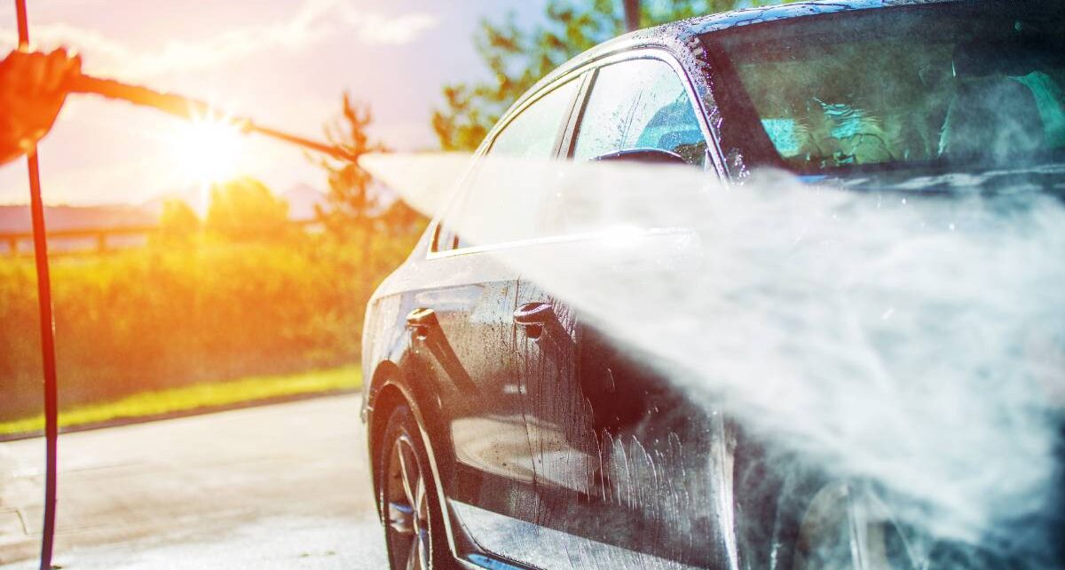 The Ideal Timelines for Cleaning Your Car Exterior 95 A car in a manual car wash getting sprayed with a jet hose sprayer. Someone is washing the car as the sun goes down.