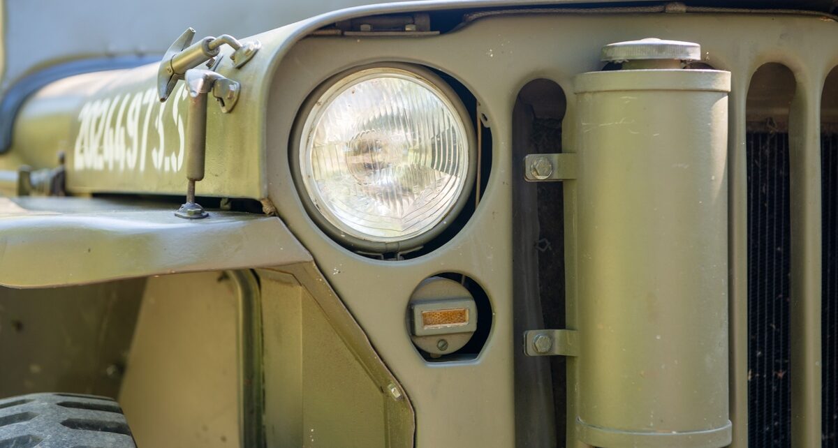 A close-up of the glass headlight and green front grille of a restored vintage Willy's Army Jeep vehicle.