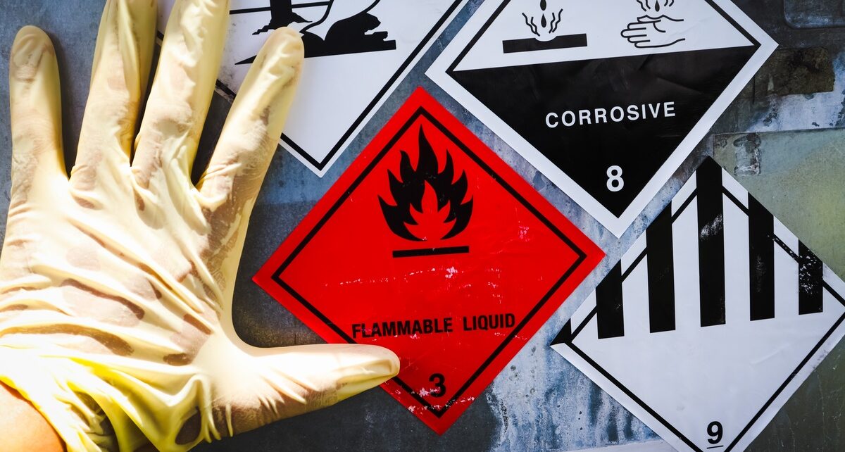 The Importance of Clear Labels for Hazardous Waste Safety 1 A hand in a dirty latex glove rests on a drum with warning labels that warn of hazardous materials and chemicals.