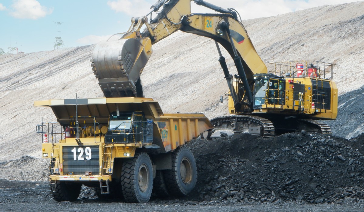 A crane is dropping coal into the bed of a dump truck. The machinery is positioned on a pile of coal.