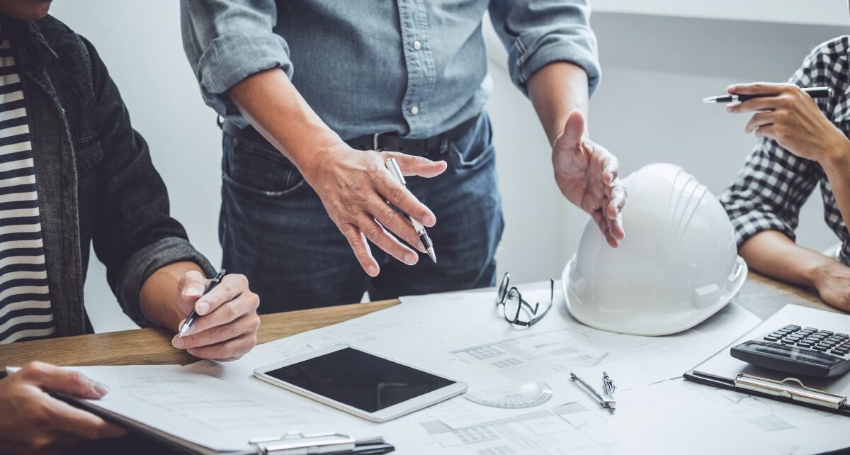 Tips for Opening a Construction Business 60 A group of people gathered around a table with papers, a white safety helmet, a calculator, and tools visible.