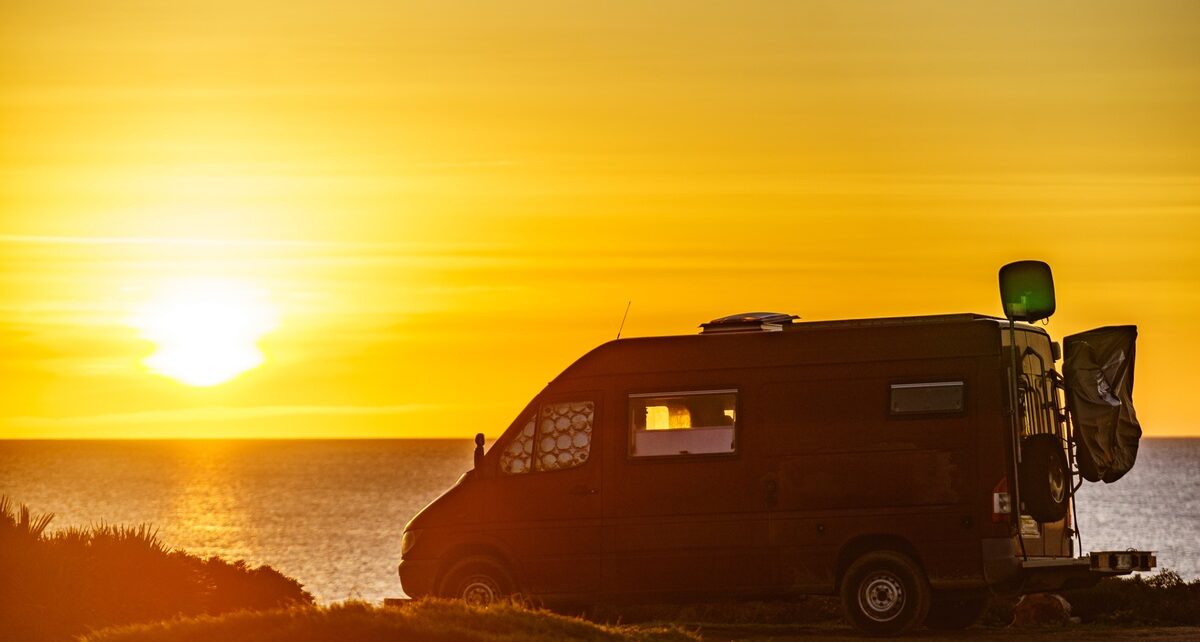 Master Sustainable Van Life: Your Weekend Travel Guide 99 A wide view of a camper van parked at the edge of a cliff, overlooking the ocean as the sun sets on the horizon.