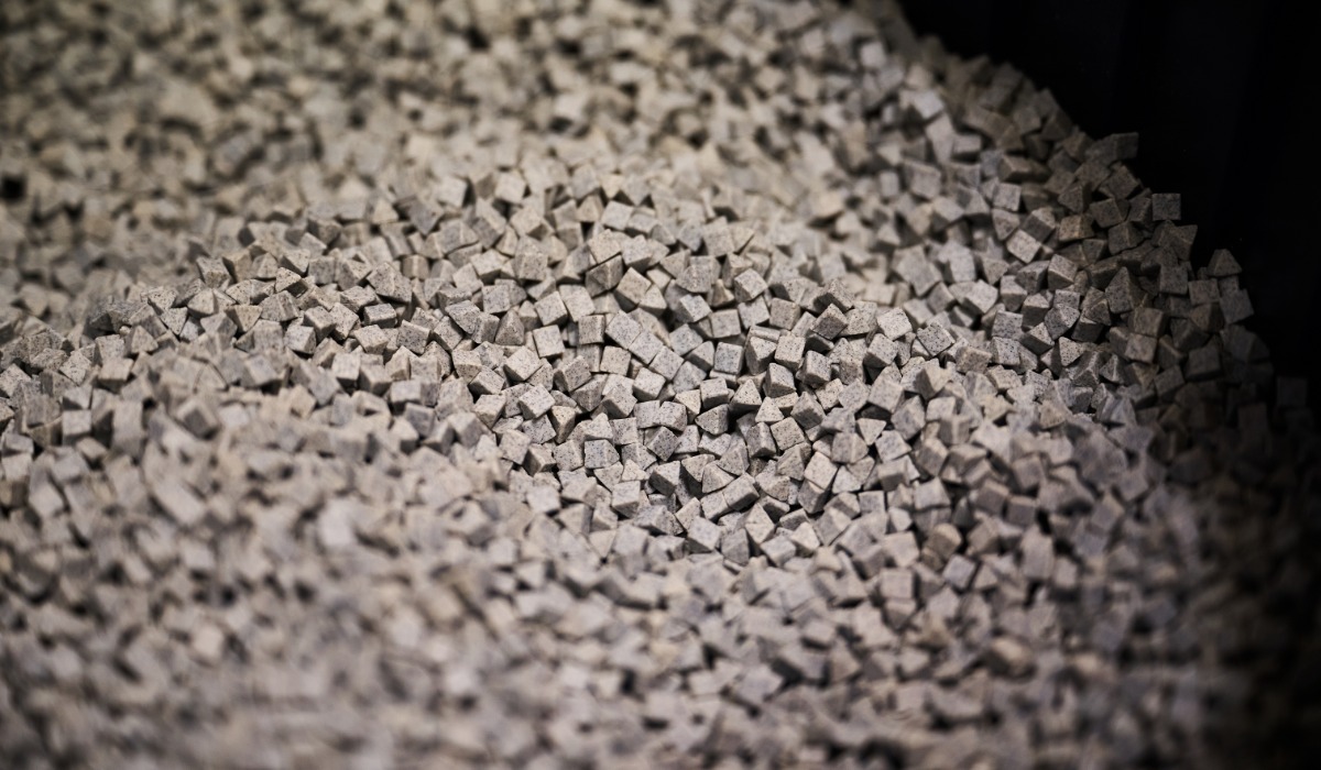 A pile of gray finishing media inside a vibratory finishing machine. Some pieces are triangles and some are squares.